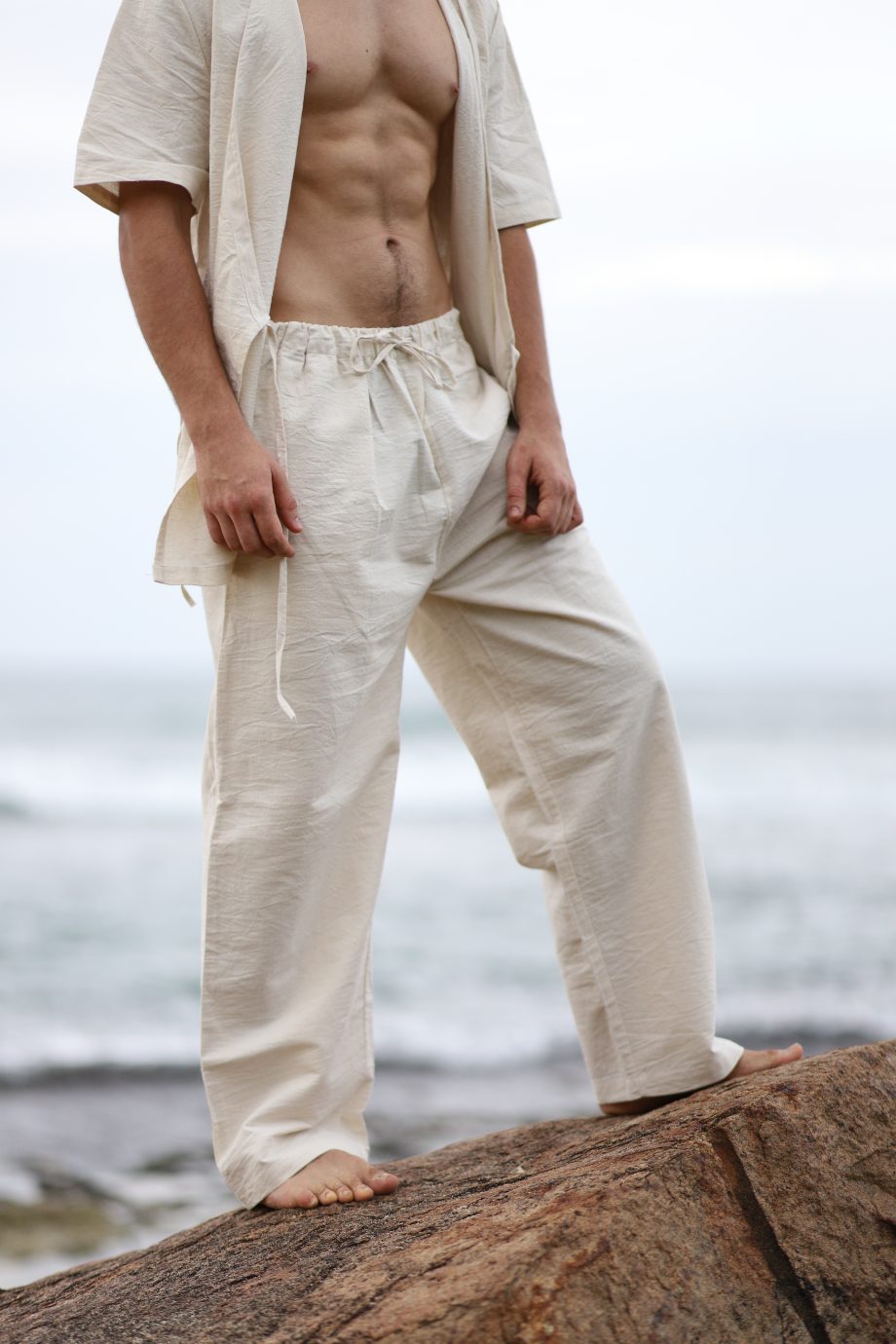 A model stands confidently in sustainable, off-white hemp pants, featuring a drawstring waist for an adjustable fit. The pants drape naturally, offering a look that's both casual and refined, perfect for diverse body types with sizes from S to XXXL.