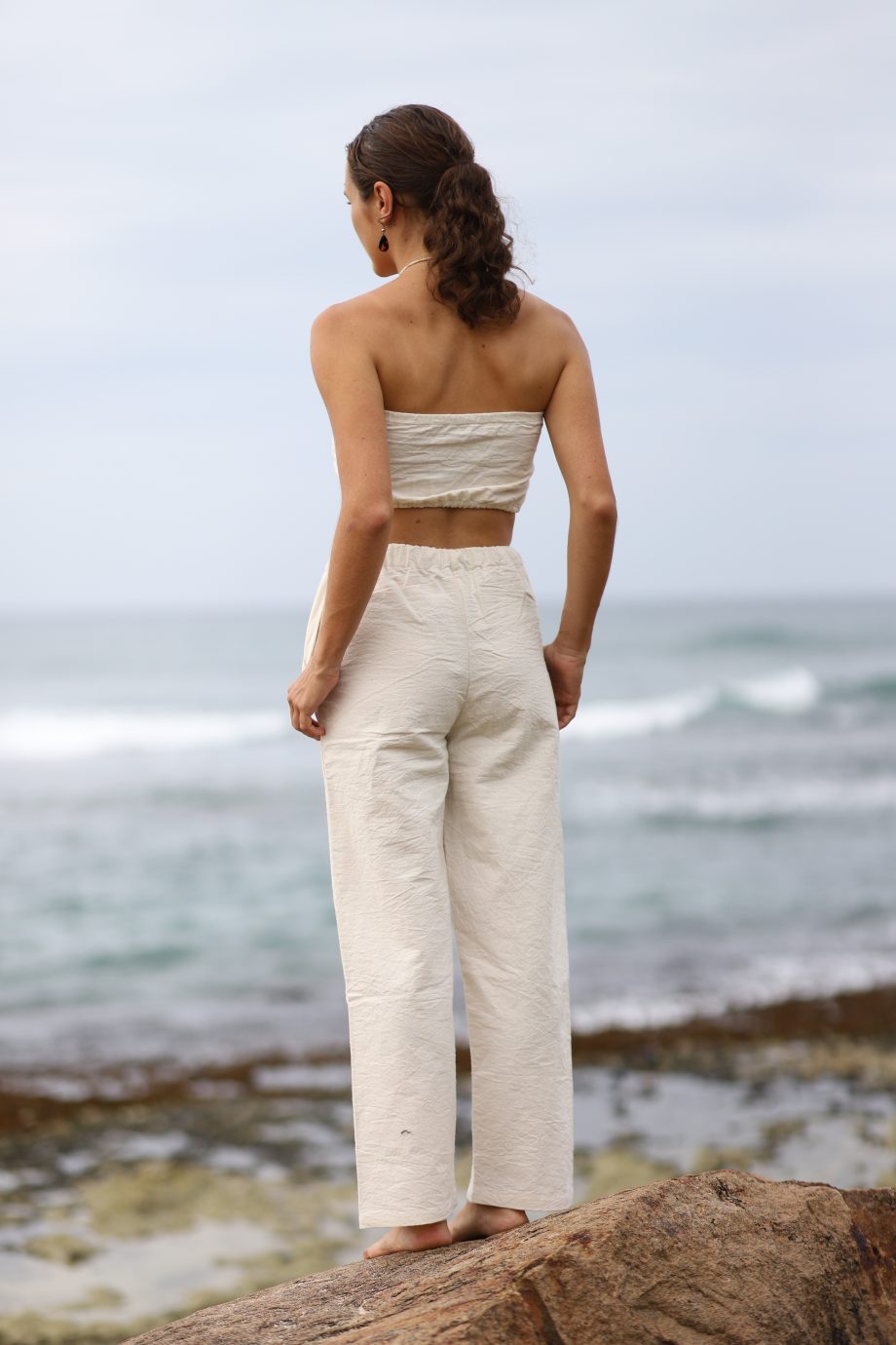 A model stands confidently in sustainable, off-white hemp pants, featuring a drawstring waist for an adjustable fit. The pants drape naturally, offering a look that's both casual and refined, perfect for diverse body types with sizes from S to XXXL.